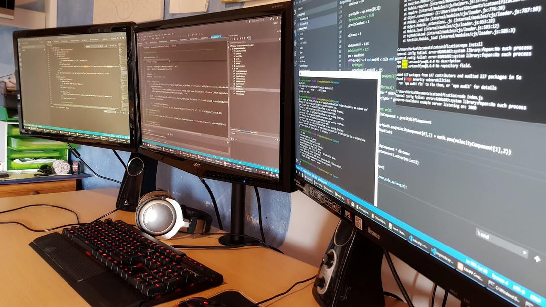 3 computer monitors showing code also a keyboard and heaphones on a desk
